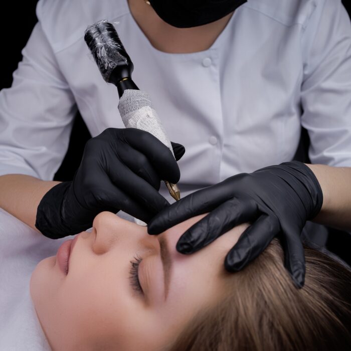 Completing permanent eyebrow makeup with a tattoo machine. PMU Procedure, Permanent Eyebrow Makeup.