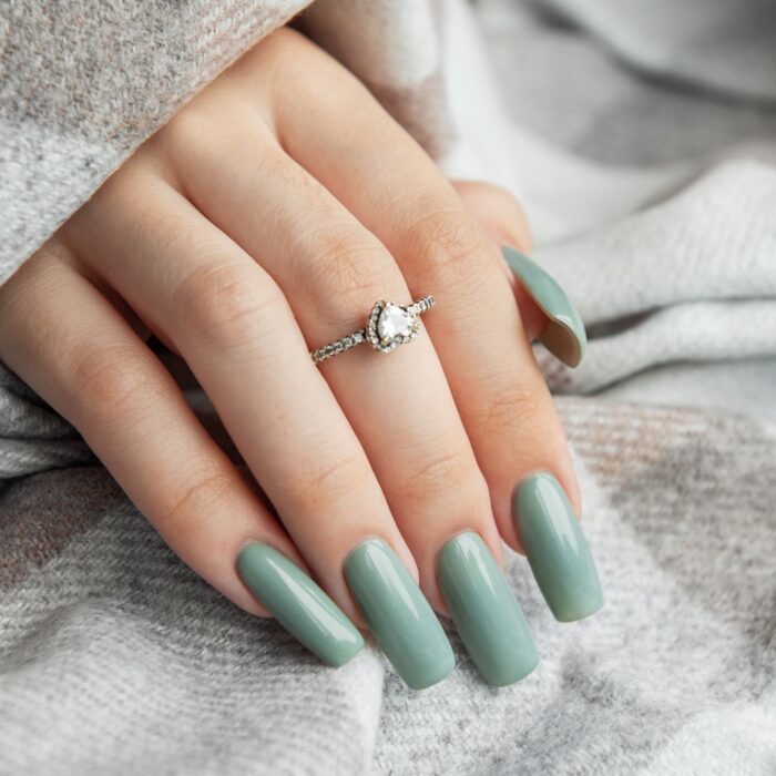 Elegant green nail polish on stylish long nails resting on a cozy blanket